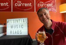 Jay holding cider in front of ESSENTIAL MUSIC READS sign